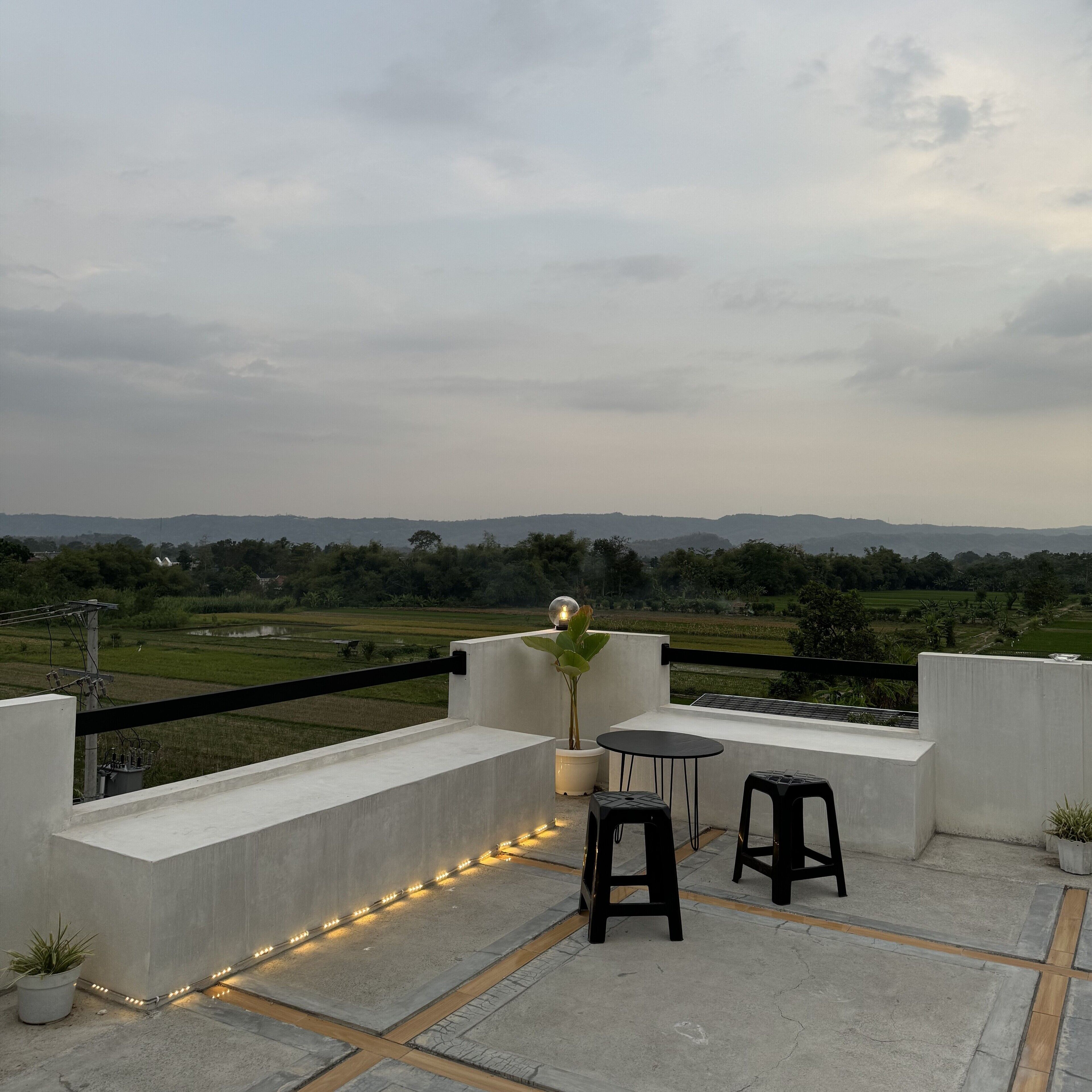 A rooftop terrace with a table and chairs, a potted plant, and a view of a green landscape.