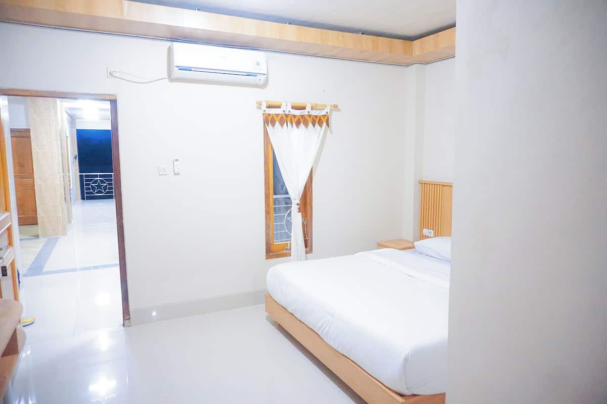 Une chambre d’hôtel comprenant un lit, une fenêtre avec des rideaux, un appareil de climatisation et une porte donnant sur une autre pièce.