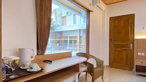 Une chambre d’hôtel avec un bureau en bois, une chaise en osier, une fenêtre avec des rideaux et une vue sur le balcon extérieur.