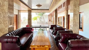 Un hall d’entrée spacieux, doté d’une longue table en bois et de canapés en cuir, de murs en marbre et de grandes fenêtres offrant une vue sur l’extérieur.