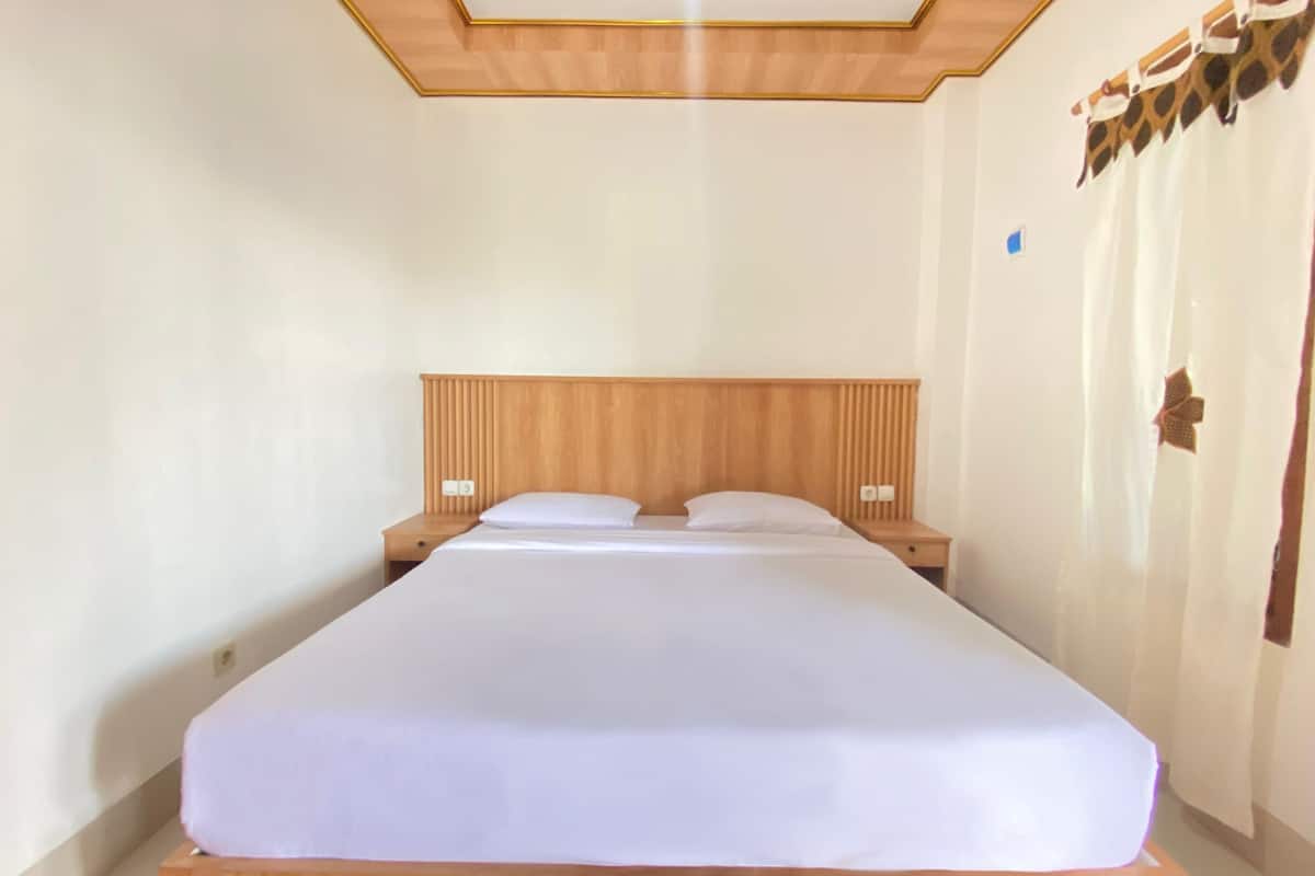 Un lit bien fait, avec une tête de lit en bois et deux tables de chevet, chacune équipée d’une lampe.