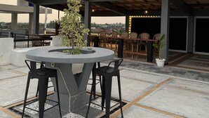 Une terrasse sur le toit avec une table ronde, des chaises et un pot de fleurs.