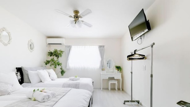 A hotel room with two beds, a desk, a TV, a ceiling fan, and a window with curtains. - Villa de Class (Osaka)