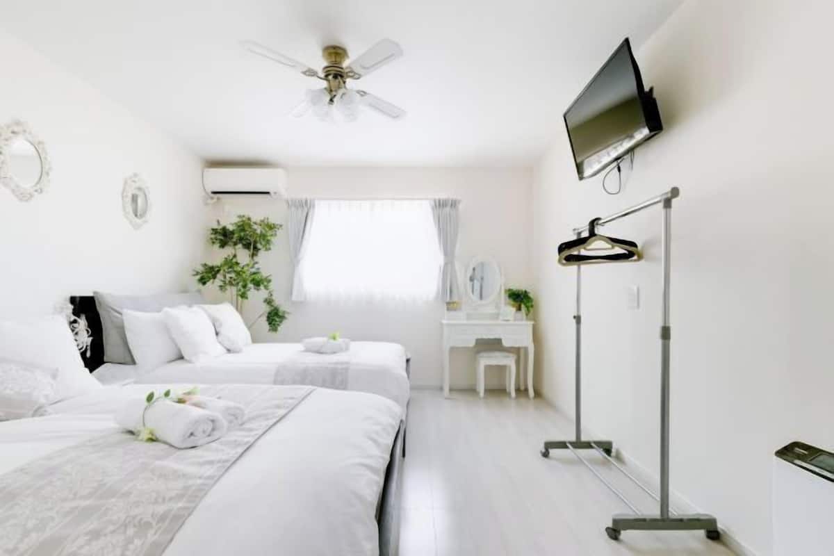 A hotel room with two beds, a desk, a TV, a ceiling fan, and a window with curtains.