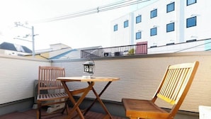 A balcony with two wooden chairs and a small table, a lantern, and a white building in the background. - Villa de Class (Osaka)