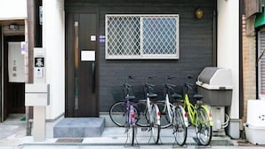 A building entrance with a dark door, a window with a metal grid, and bicycles parked outside. - Villa de Class (Osaka)