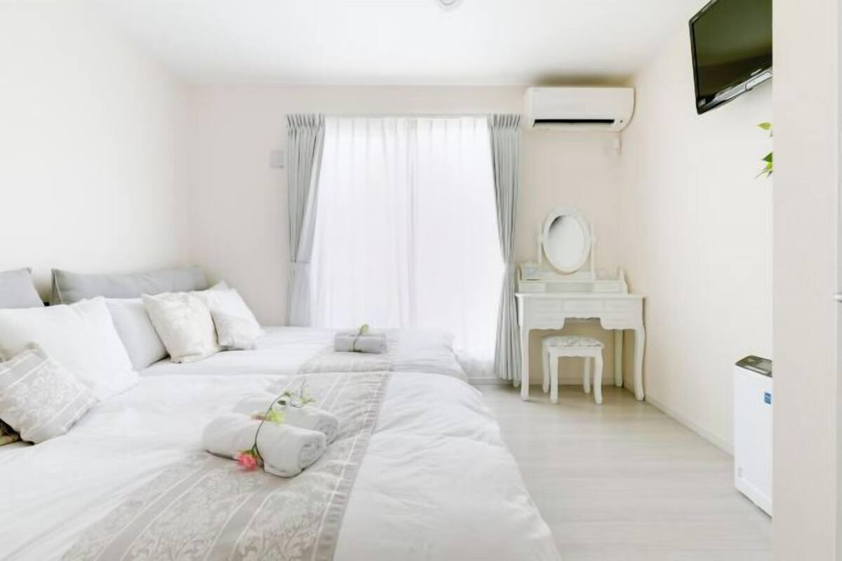 A hotel room with a bed, a vanity with a mirror, a desk, and an air conditioning unit.
