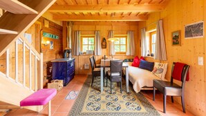 Interior acogedor de una cabaña de madera con escalera, comedor y sala de estar con sofá y sillones.