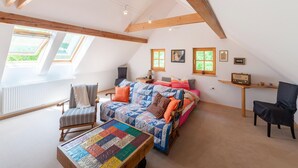 Un dormitorio acogedor en el ático, con techo inclinado, vigas de madera, una cama con colcha colorida, una mesita con una radio y una silla.