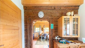Un interior rústico de madera con una zona de cocina que incluye armarios, una mesa de comedor y un reloj en la pared.