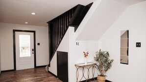 Eine Treppe mit schwarzen Geländern führt zu einer Zwischenebene. Dort steht ein Blumentopf, in der Nähe ein kleiner Tisch mit einer Blumenvase.