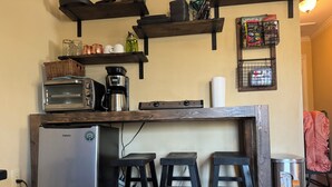 Une cuisine compacte équipée d’un réfrigérateur Galanz, d’une machine à café, d’un grille-pain et d’une poubelle à pédale. On y trouve également deux tabourets et une poubelle.
