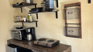 Une cuisine compacte avec un plan de travail en bois, une cuisinière, un grille-pain et un réfrigérateur. On y trouve deux tabourets et un panier suspendu au mur.