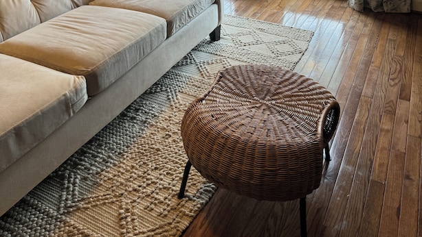 Un salon chaleureux avec un canapé beige, un fauteuil en osier et une grande fenêtre agrémentée de rideaux.