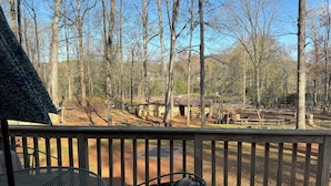 Une terrasse en bois avec une table et des chaises en métal, donnant sur un espace clos planté d’arbres et bordé d’un bâtiment.