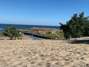 Une plage de sable avec un petit étang, des affleurements rocheux et des arbres.