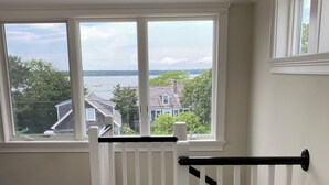 Une pièce dotée d’un plancher en bois, d’une rambarde blanche et offrant une vue sur une étendue d’eau et des maisons, grâce à de grandes fen êtres.