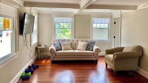 Un salon spacieux avec un canapé beige, un fauteuil assorti et un téléviseur à écran plat fixé au mur.