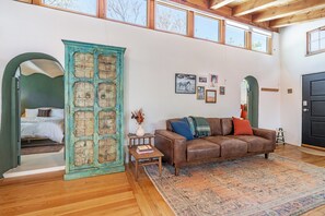 A spacious living room with a brown leather sofa, a patterned rug, and a rustic blue cabinet. - Stunning Artful Adobe - Super Walkable Location (Santa Fe)