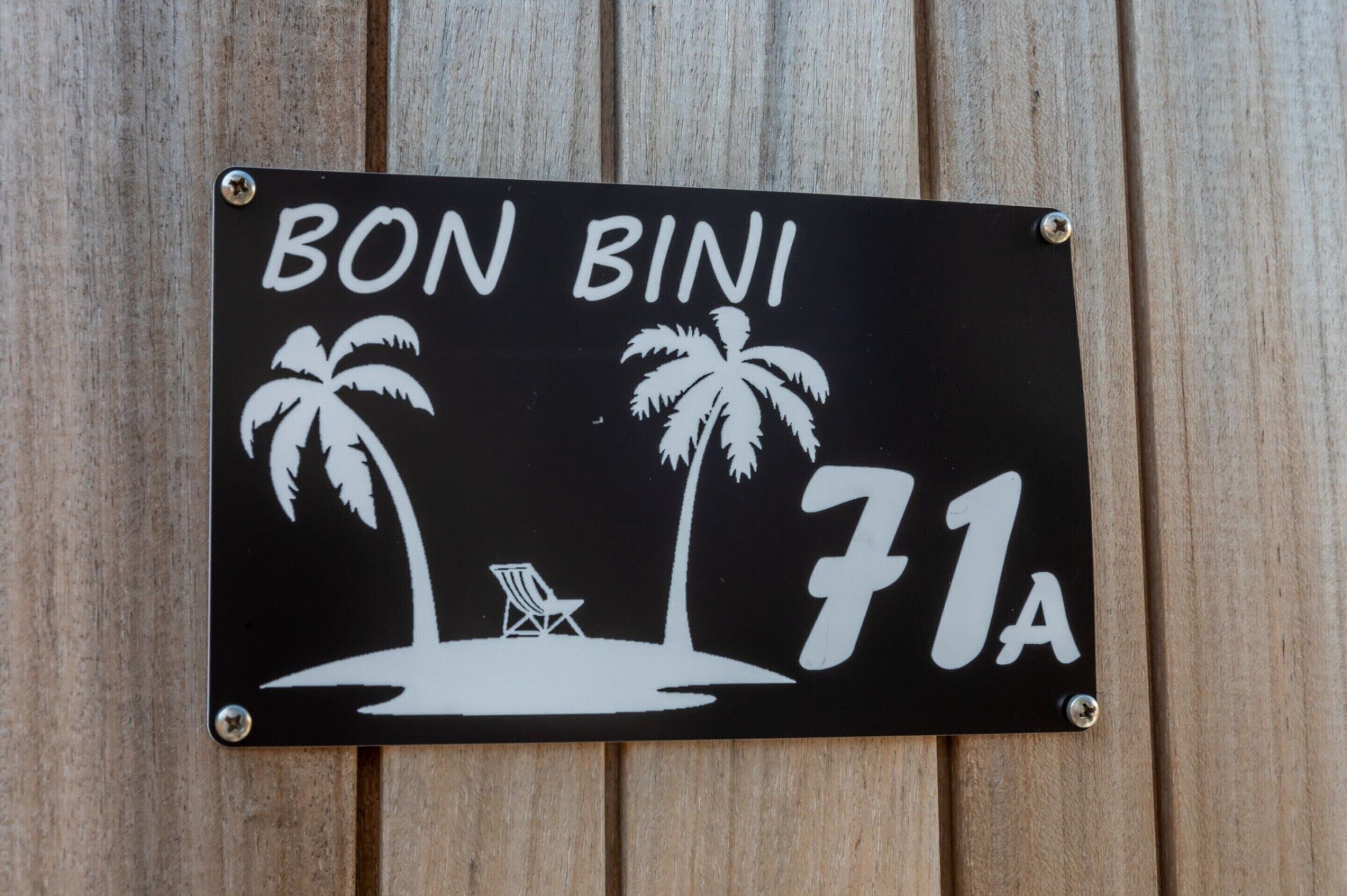 Musta kyltti, jossa on valkoista tekstiä ja palmujen kuvia. Kyltissä lukee nimi ”BON BINI” ja numero ”71A”.