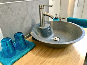 Une salle de bain moderne avec un grand lavabo sur pied, un robinet et deux récipients en verre bleu posés sur un comptoir en bois.