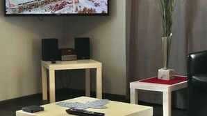 A living room with a flat-screen TV mounted on the wall, two small tables, a sofa, and a decorative vase. - Holiday Apartment Erlebnisrhoen (Ehrenberg)