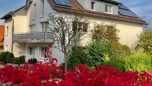 A two-story house with solar panels on the roof, a balcony, and a garden with red foliage. - Holiday Apartment Erlebnisrhoen (Ehrenberg)