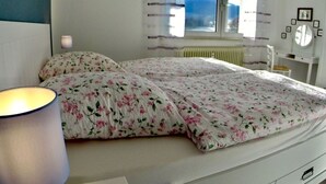 A bedroom with a bed, a bedside lamp, a window with curtains, a radiator, and a dresser with a mirror. - Holiday Apartment Erlebnisrhoen (Ehrenberg)