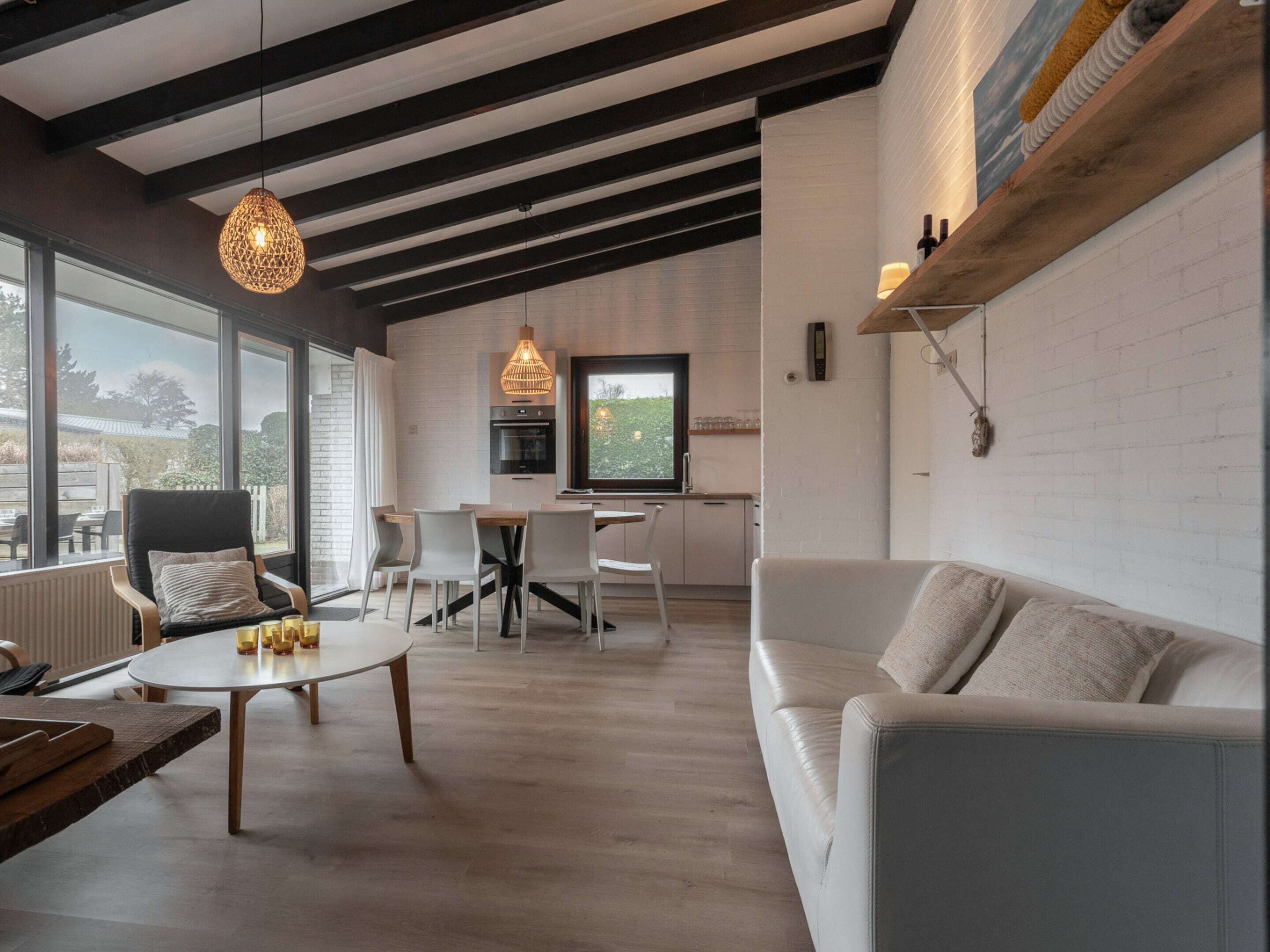 A modern living room with a large window, a dining area, and a kitchen.