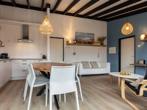Une cuisine moderne avec des meubles blancs, une table à manger en bois et des chaises blanches. Le salon comprend un canapé blanc et une petite table en bois avec des chaises.