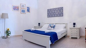 Un dormitorio ordenado con cama, mesitas de noche, una lámpara y una pared decorada con cuadros.