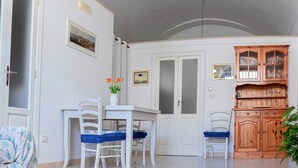 Un comedor con una mesa y sillas blancas, un mueble con puertas de cristal y una puerta con paneles de vidrio satinado.