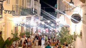 Un área de comedor al aire libre con mesas y sillas, rodeada de edificios con balcones y detalles decorativos.