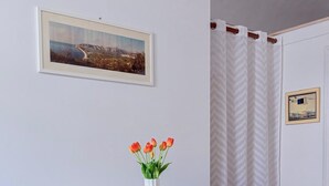 Mesa blanca con dos sillas, un florero, un cuadro en la pared y una ventana con cortinas.