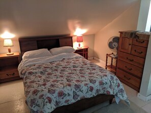 A bedroom with a bed, two bedside lamps, a wooden dresser, and a floor fan. - BIG Comfy Lakefront cottage, Clear Lake by Huntsville, north Muskoka! (Emsdale)
