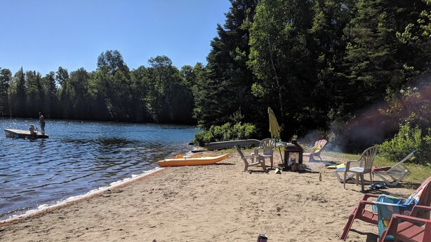 Una playa junto al lago con kayak, sillas y un bote pequeño.