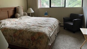 Una camera d'albergo con un letto, una sedia, un comodino, una lampada e una finestra vista alberi.