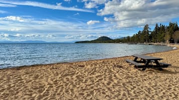 Une plage de sable avec une table de pique-nique, une eau calme et, au loin, une île couverte de forêts.