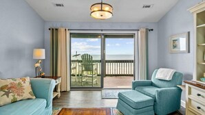 A room with a view of the sea, a sofa, a chair, and a lamp.