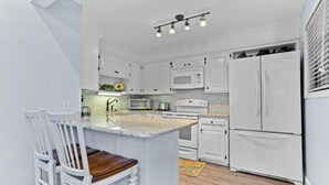 A kitchen with white cabinets, a central island, a microwave, a stove, and a refrigerator.