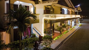 A two-story hotel with a balcony, outdoor plants, and a well-lit entrance. - HOTEL SIERRA ARENAL - QUADRUPLE ROOM  (Alajuela)