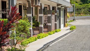 A modern building with a covered porch, potted plants, and a gravel driveway. - HOTEL SIERRA ARENAL - QUADRUPLE ROOM  (Alajuela)