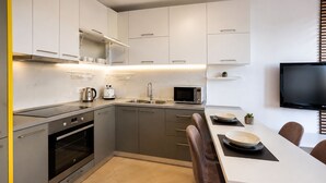 Una cocina moderna con horno empotrado, microondas y lavabo, una zona de comedor con mesa y sillas, y un televisor de pantalla plana montado en la pared.