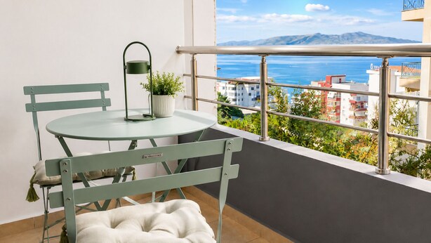 Un balcón con una mesa redonda y sillas, una planta en maceta y vistas al mar y edificios.