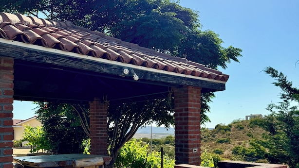 A covered outdoor seating area with a brick table and chairs, surrounded by greenery and a vineyard in the background. - Cabañas Colibri (Valle de Guadalupe)