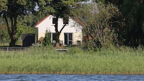 A white house with a red roof, surrounded by tall grass and trees, near a body of water. - Holiday Home Reed Path (Warin)