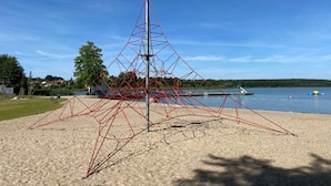A geometric metal sculpture on a sandy beach with a lake and houses in the background. - Holiday Home Reed Path (Warin)