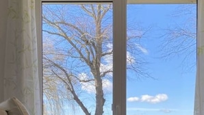 A room with a large window offering a view of a tree and a body of water. - Holiday Home Reed Path (Warin)