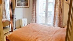 Een slaapkamer met een bed, een raam met gordijnen, een radiator en een schilderij aan de muur.