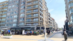 Een meerlaags woongebouw met balkons, een overdekt terras en een voetpad.